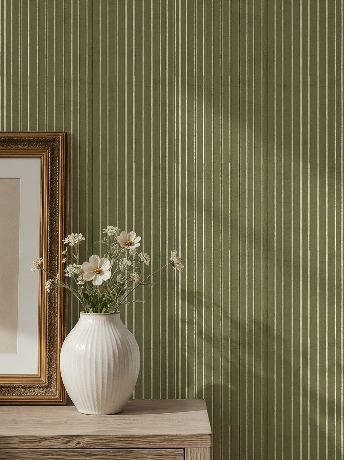 Olive green and dusty pink striped wallpaper in a vintage room setting with a vase and framed art.